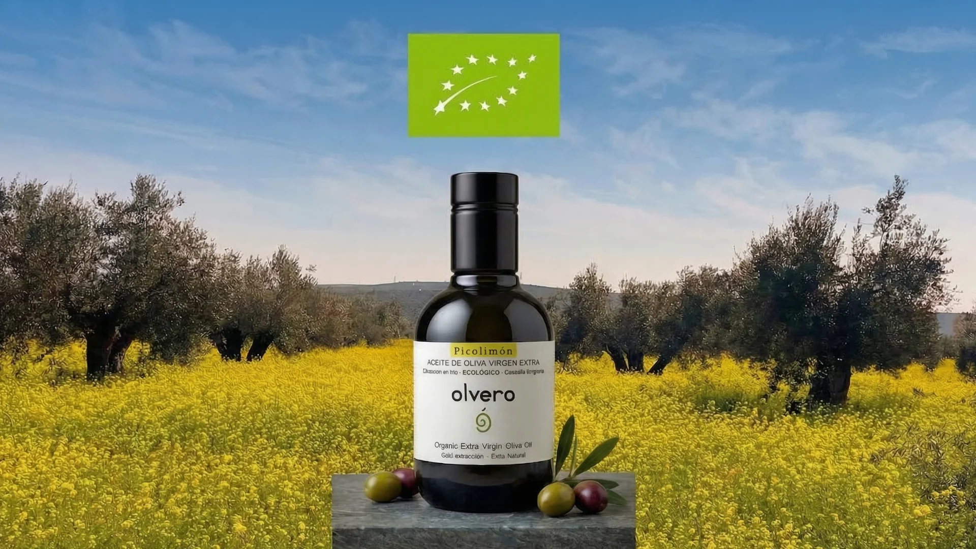 Botella de aceite de oliva virgen extra ecológico Olvero con hojas de olivo en fondo de olivar ecologico